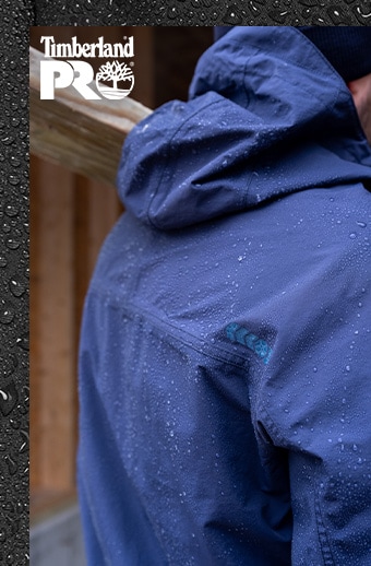 Image of a man wearing a blue Timberland PRO water resistant jacket. You can see his back and water drops on the jacket. 