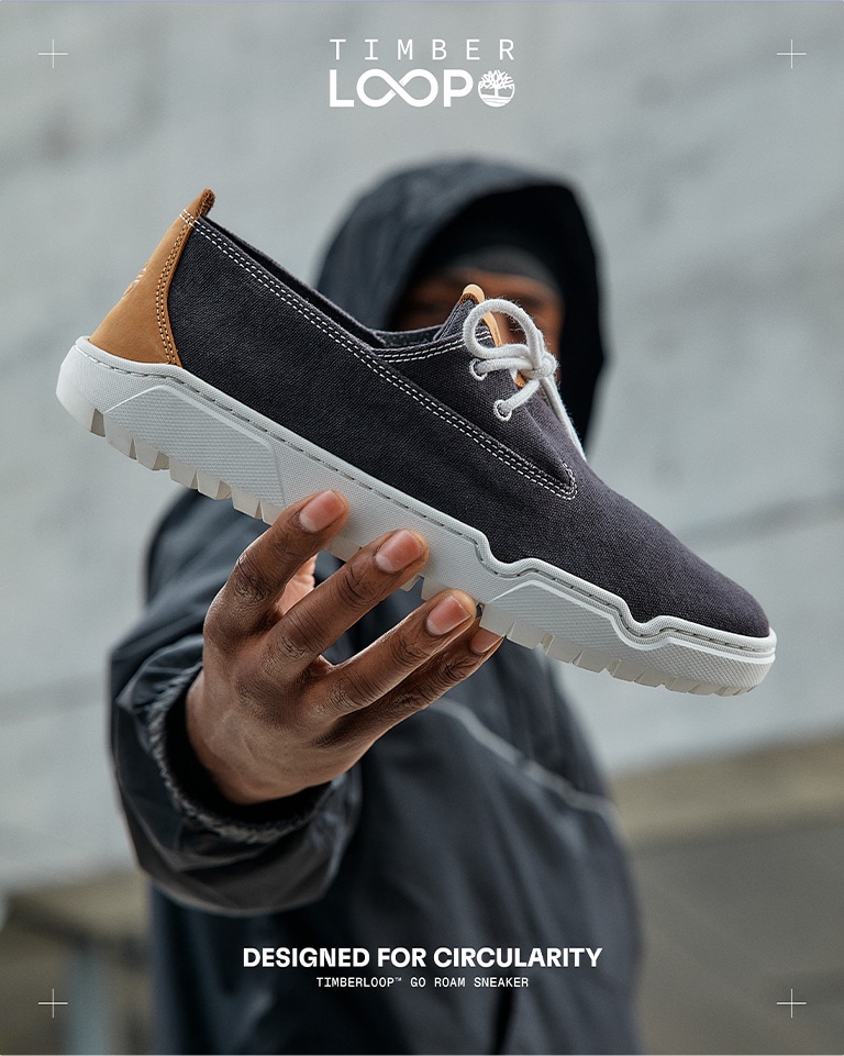 Image of a man wearing a hoodie holding a sneaker with one hand out in front of him